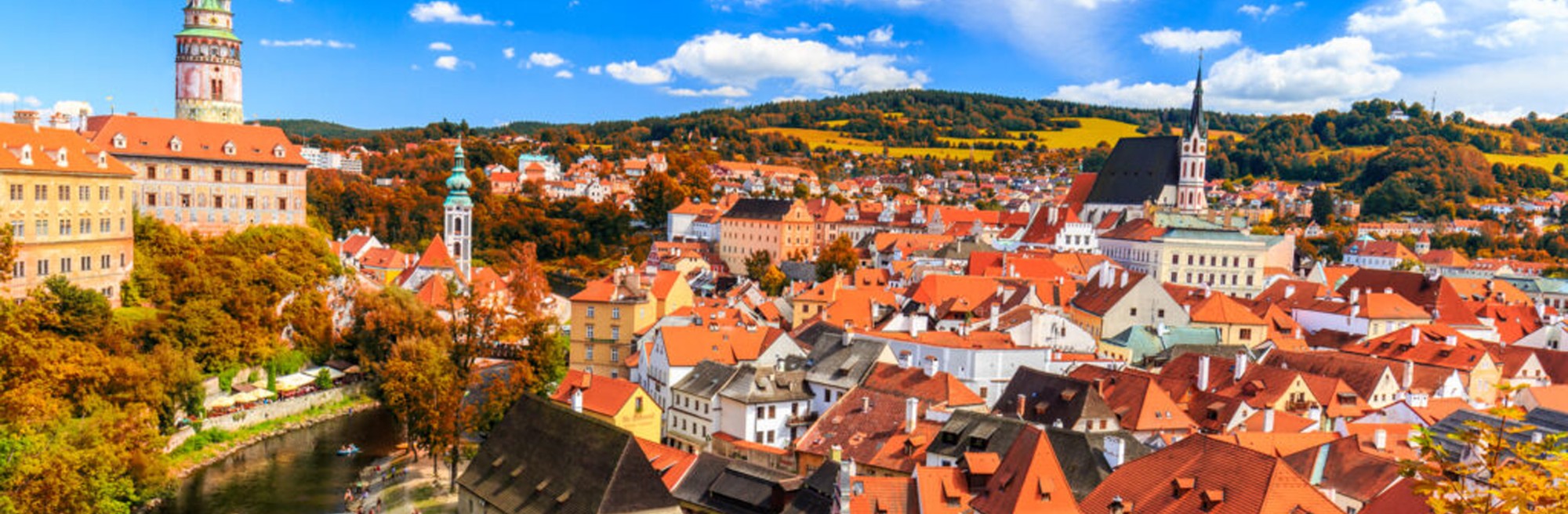 A historic Czech town in autumn: red-tiled roofs, church spires and a castle tower above the river